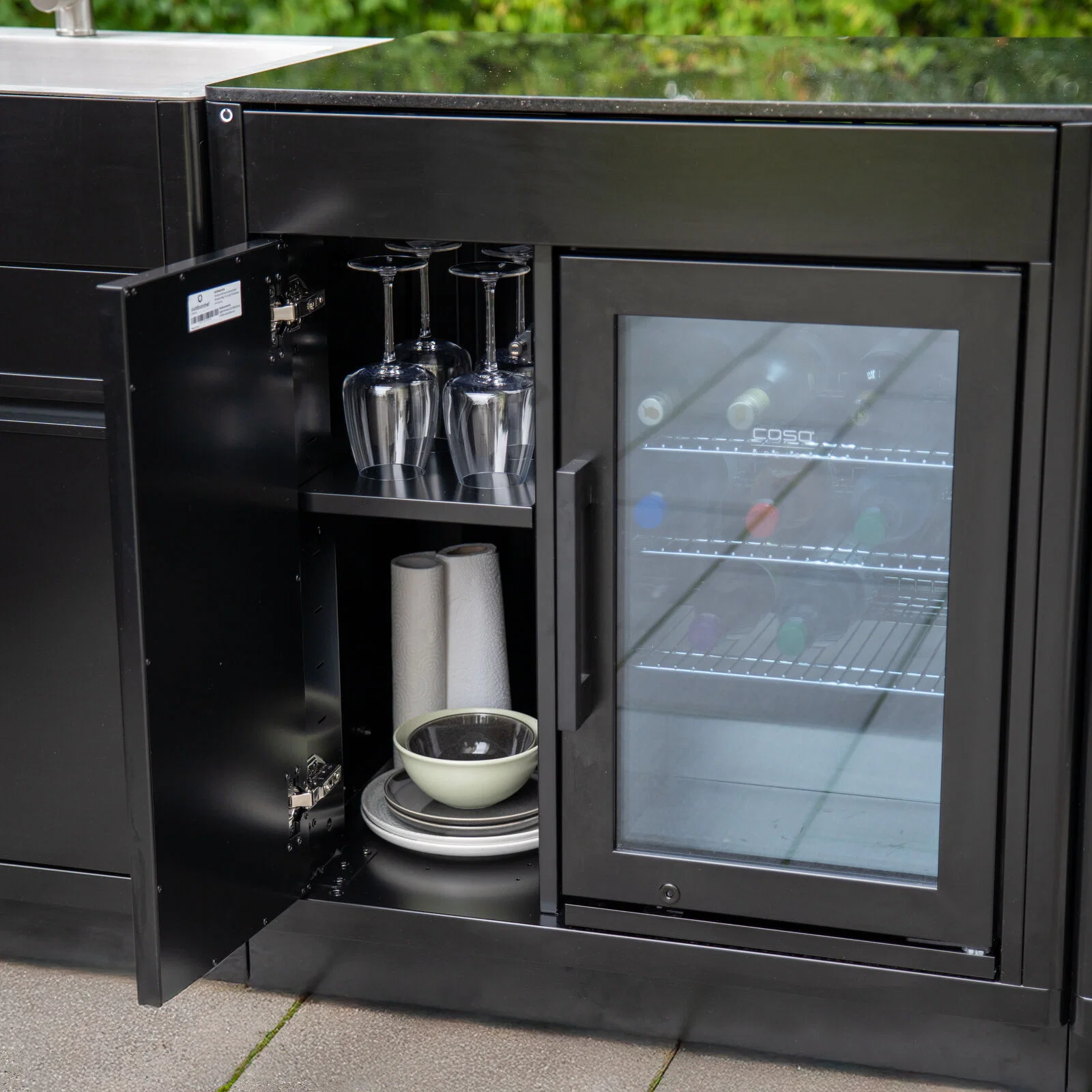 Geöffnetes Stauraumfach neben dem Caso BBQ Cooler mit Gläsern und Geschirr